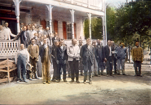 Men stand out front of a building in a hand-colored photograph